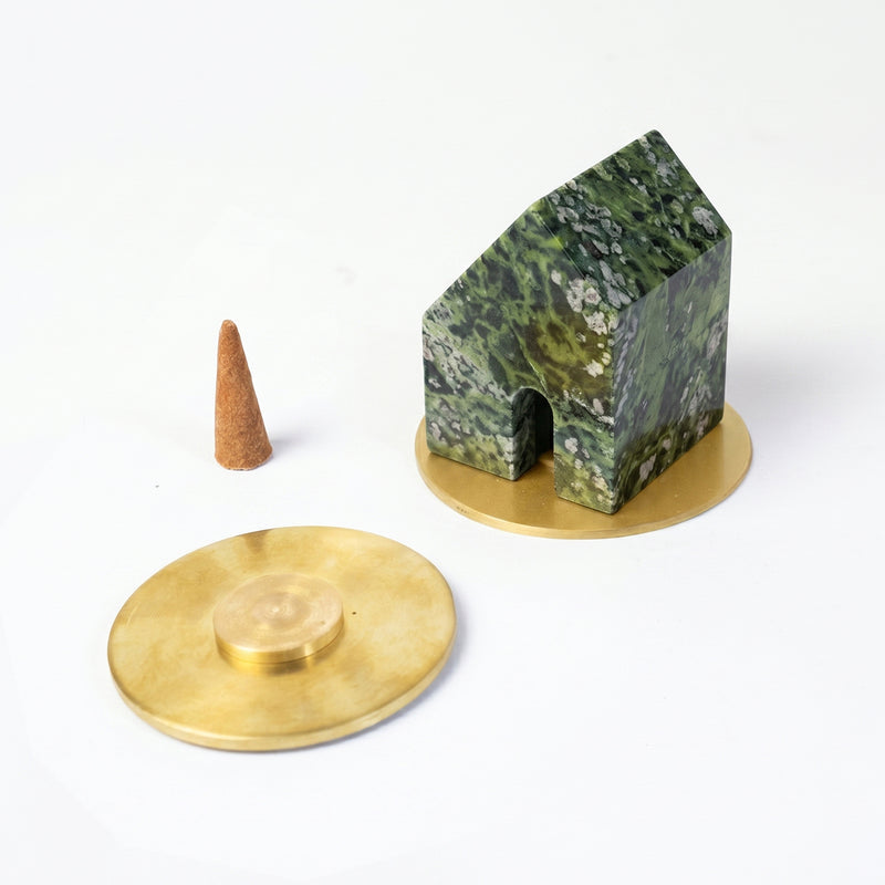 Green serpentine house-shaped incense holder resting on a gold base. Next to it lies a loose incense cone and a second gold base against a clean white background.