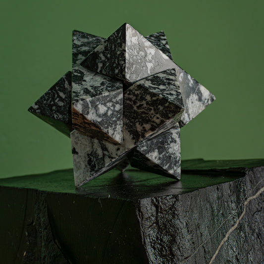 Geometric zebra jasper star, made of precisely proportioned interlocking pieces, resting on a dark block against a green background.