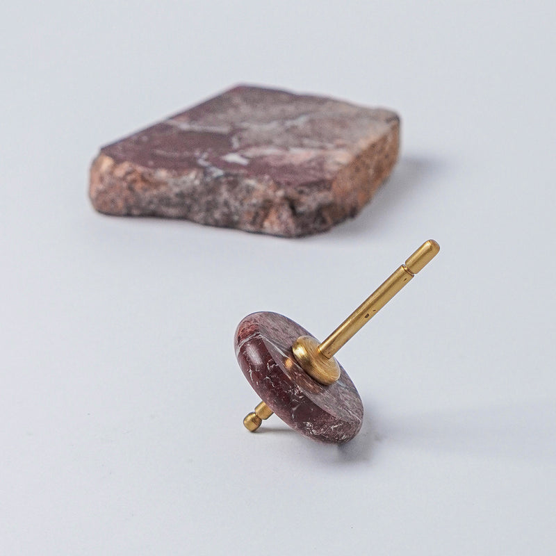 Spinning top with a polished red jasper disc and gold spindle, resting on a white background next to a raw block of the same stone.