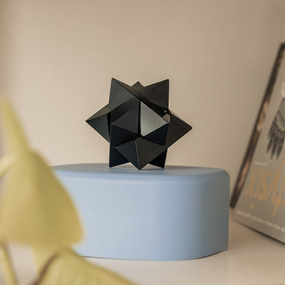 Black onyx stone burr puzzle resting on a textured surface in a quiet luxury setting.