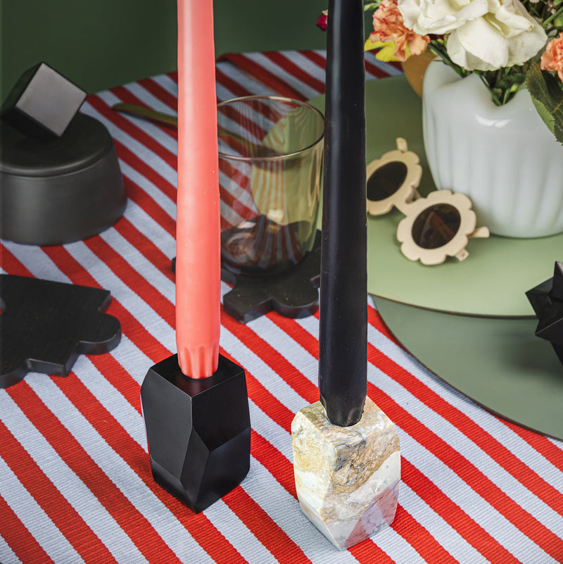 Two candles in gemstone faceted soapstone and black candle holders on a red and white striped tablecloth with decorative items in the background.