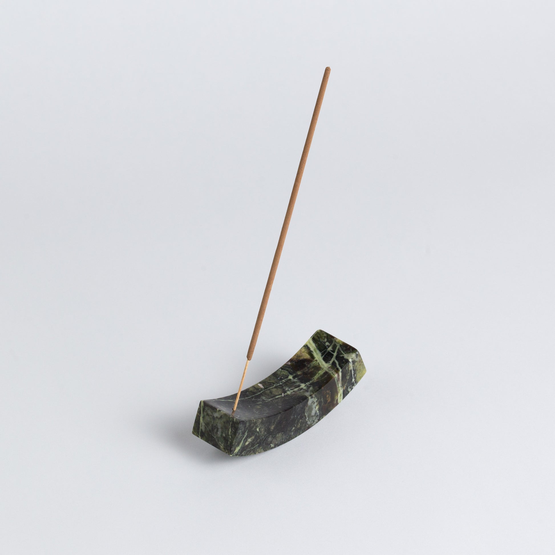 Smooth, handcrafted serpentine stone curved incense holder on a white background.