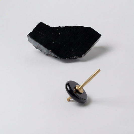 Spinning top with a polished black onyx disc and gold spindle, resting on a white background next to a raw block of the same stone.