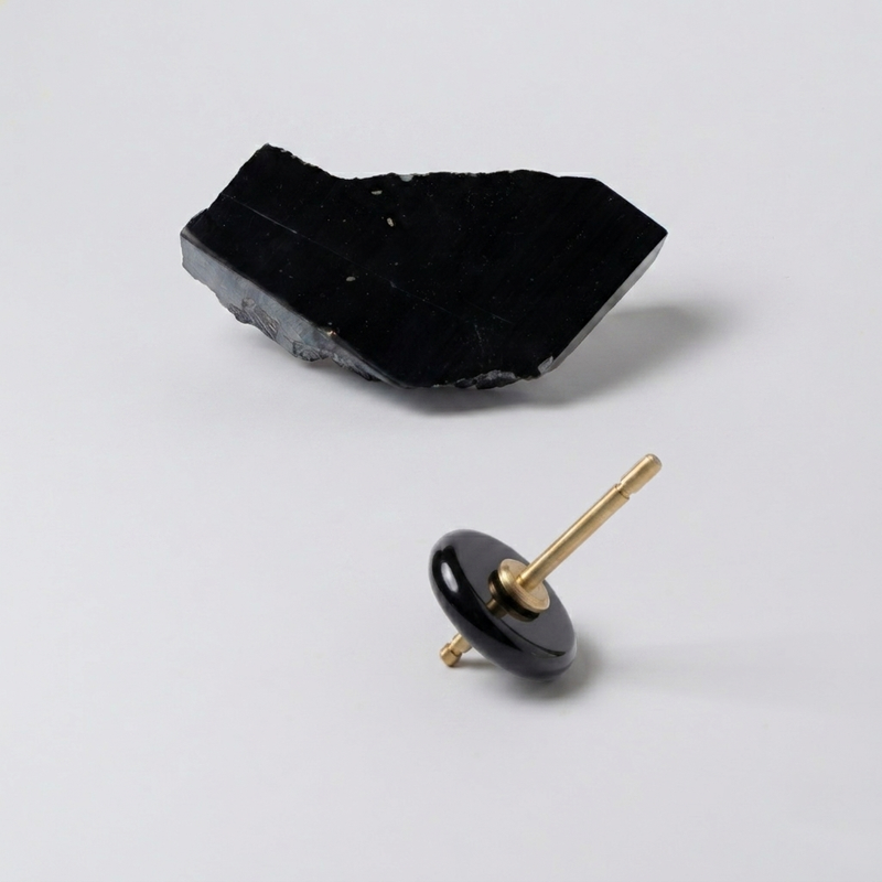 Spinning top with a polished black onyx disc and gold spindle, resting on a white background next to a raw block of the same stone.