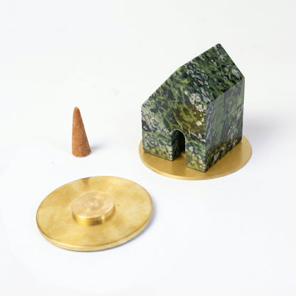 Green serpentine house-shaped incense holder resting on a gold base. Next to it lies a loose incense cone and a second gold base against a clean white background.