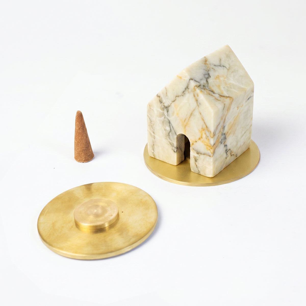 Creamy soapstone house-shaped incense holder resting on a gold base. Next to it lies a loose incense cone and a second gold base against a clean white background.