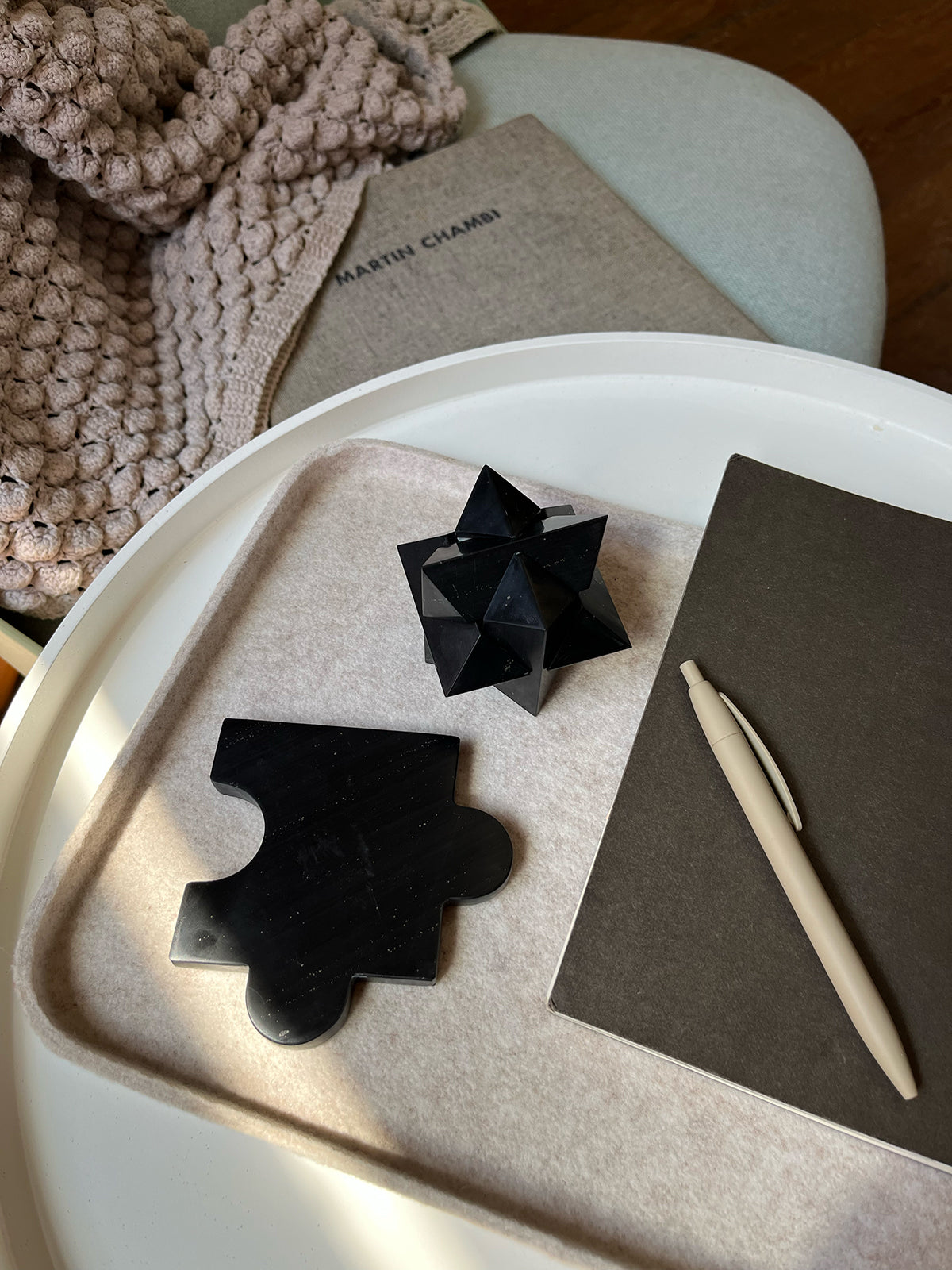 Black star-shaped puzzle and puzzle coaster on a tray with a pen and notebook