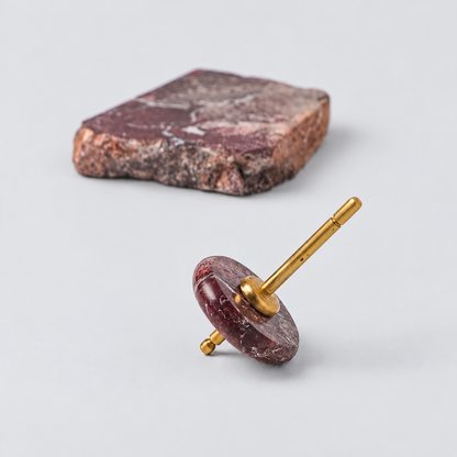 Spinning top with a polished red jasper disc and gold spindle, resting on a white background next to a raw block of the same stone.