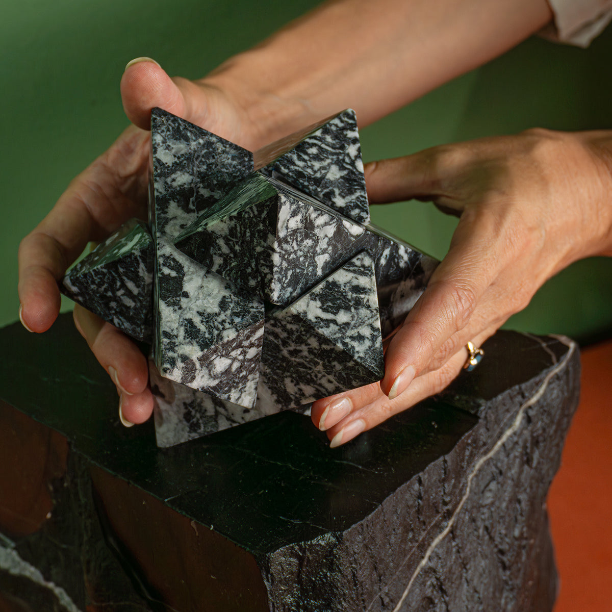Two hands holding a large zebra jasper star, showing the scale and volume of its geometric proportions over a dark base.