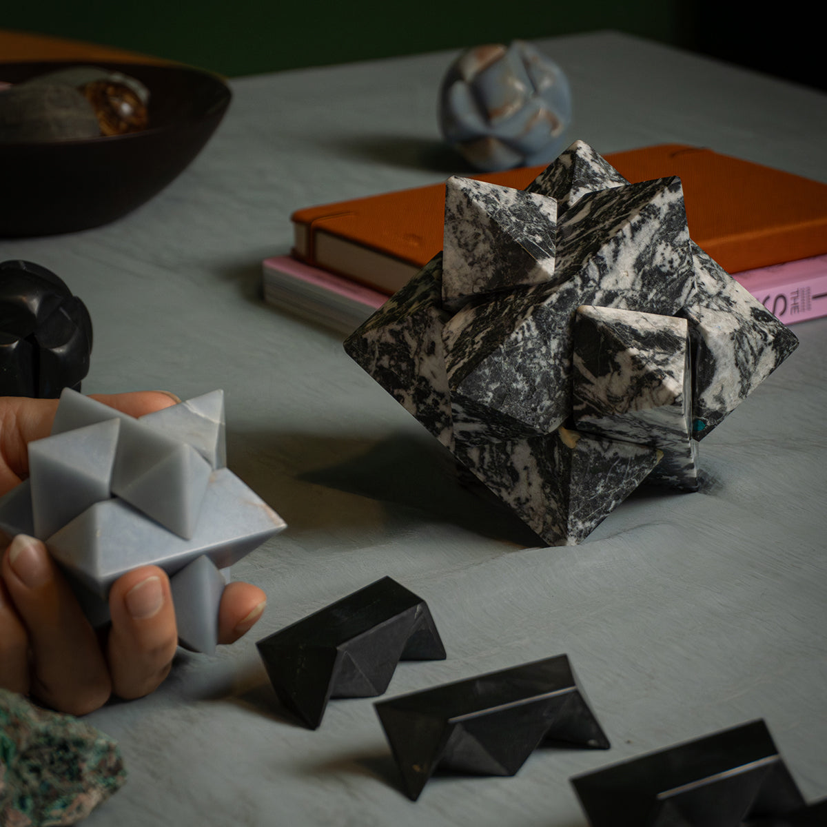 A hand holding an angelite star, showing the difference in proportions compared to a zebra jasper version and other disassembled pieces on the table.