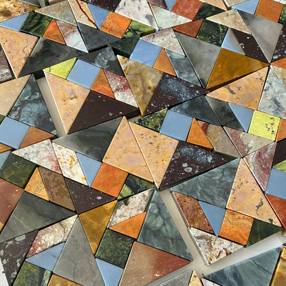 Close-up of multiple triangular natural stone pieces placed together. The details, veins, and different earthy, green, and blue tones of each block can be seen.
