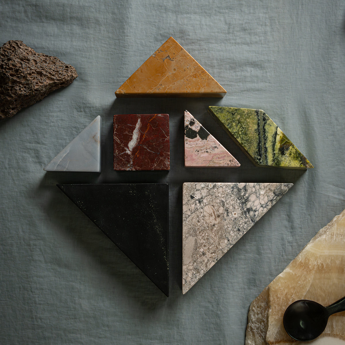 The seven puzzle pieces separated and arranged in the shape of a house on a grayish-blue fabric. There are rustic decorative stones on the sides.