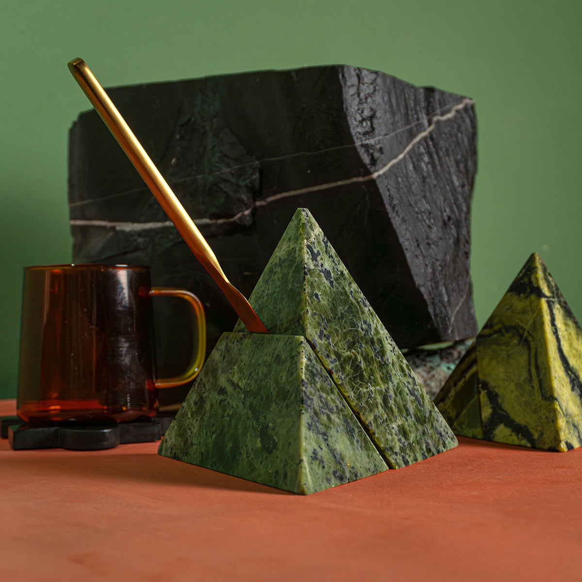 Two hands adjusting the pieces of a geometric deep green nephrite pyramid. The figure rests on a stack of books under natural light that highlights its interlocking joints.