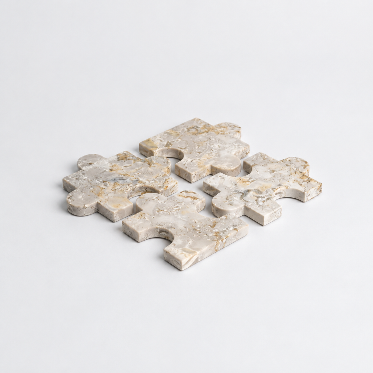 Four interlocking jigsaw puzzle pieces made of polished stone, featuring a natural beige and light gray marbled pattern with subtle gold veining, set against a clean white background.