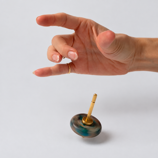 A hand suspended over a green nephrite spinning top with a gold spindle, spinning rapidly on a white background, showing the visual motion blur of the stone.