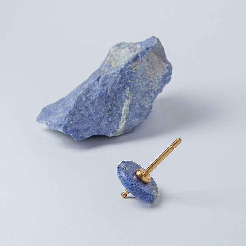 Spinning top with a polished blue dumortierite disc and gold spindle, resting on a white background next to a raw block of the same stone.