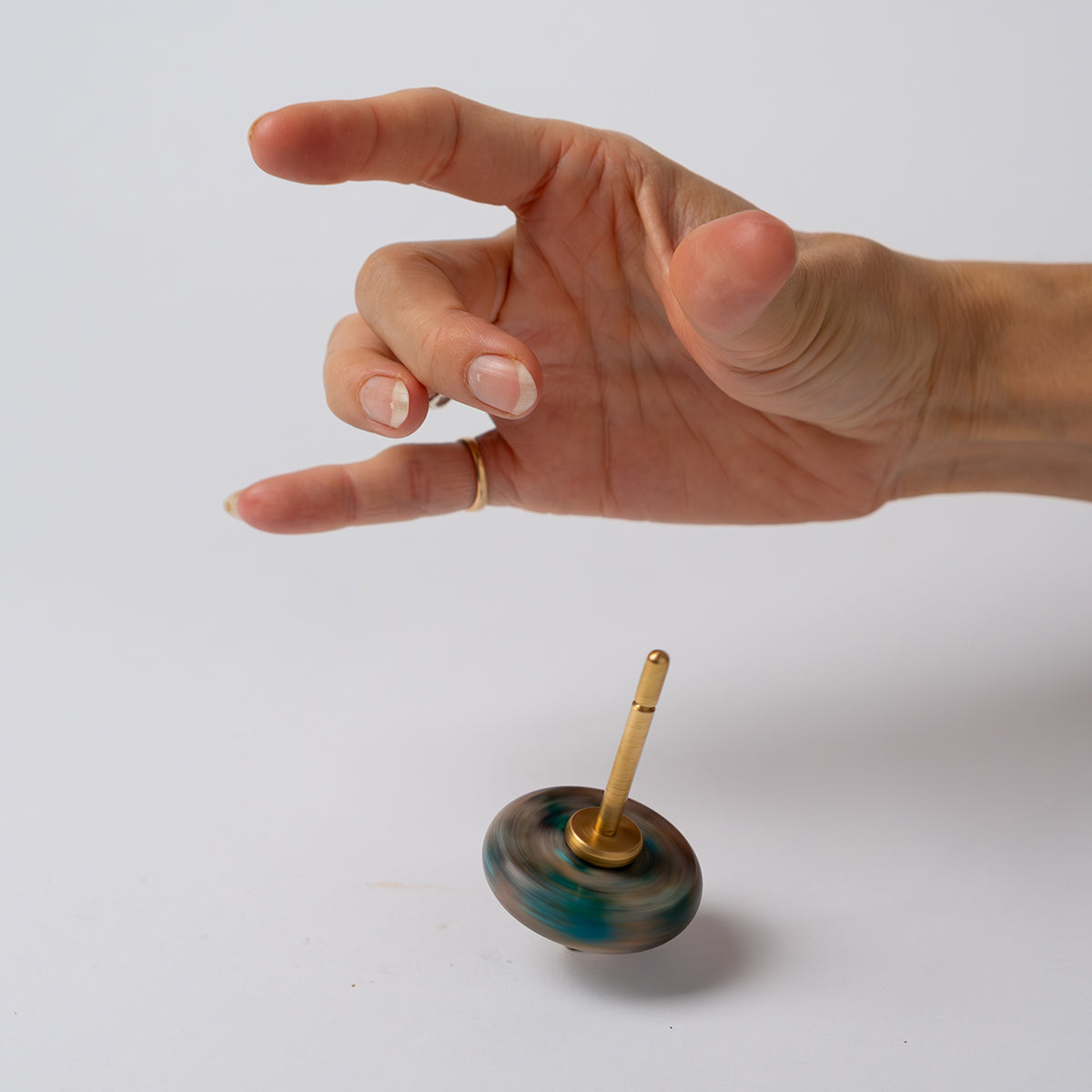 A hand suspended over a green nephrite spinning top with a gold spindle, spinning rapidly on a white background, showing the visual motion blur of the stone.