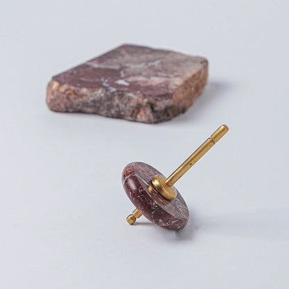 Spinning top with a polished red jasper disc and gold spindle, resting on a white background next to a raw block of the same stone.